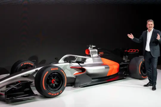 Ein Mann präsentiert stolz ein futuristisches Formel 1 Auto in Silber und Orange.