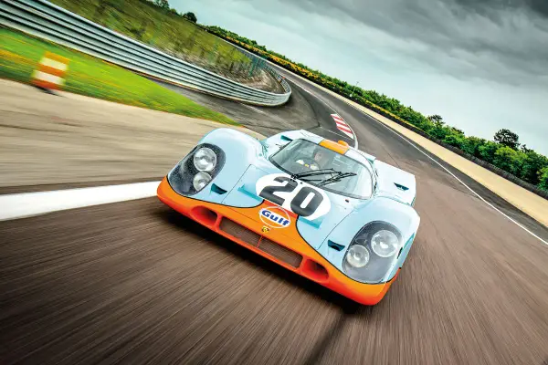 Ein ikonischer Porsche Rennwagen aus den 80ern, der Gulf-Porsche 917, rast auf einer Rennstrecke.