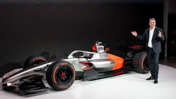 Ein Mann präsentiert stolz ein futuristisches Formel 1 Auto in Silber und Orange.