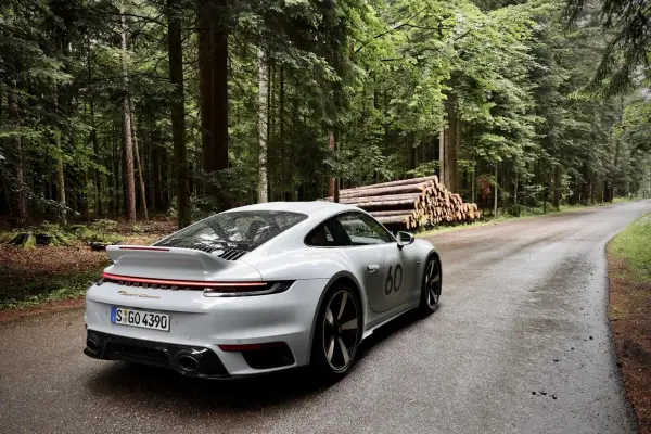 Ein weißer Porsche 911 mit der Nummer 60 auf der Seite fährt auf einer nassen Waldstraße. Die Beschleunigung von 0 auf 100 km/h ist beeindruckend.