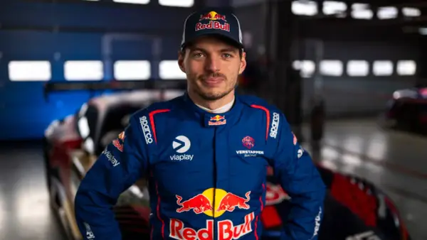 Max Verstappen im Rennanzug, bereit für das 24h Rennen. Sein Blick ist fokussiert, die Red Bull-Logos sind deutlich sichtbar.