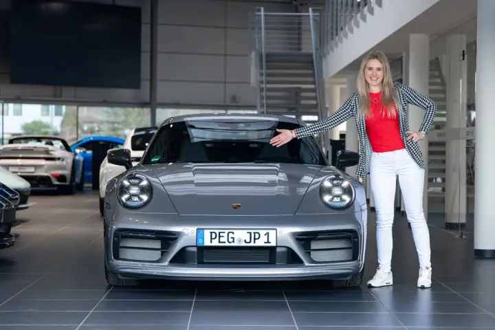 Eine Frau präsentiert stolz einen grauen Porsche Carrera T. Die Wertentwicklung dieses Sportwagens ist ein spannendes Thema für Enthusiasten.