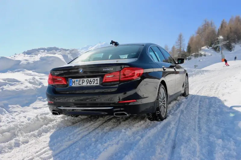 Schwarzer BMW 540i G30 fährt durch tiefen Schnee auf einer Skipiste, bergauf mit Skilift im Hintergrund.