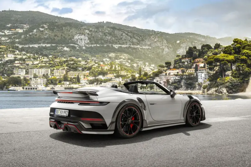 Ein weißer Techart GTstreet RS Cabriolet steht an einer Küstenstraße mit Blick auf eine malerische Stadt am Hang.