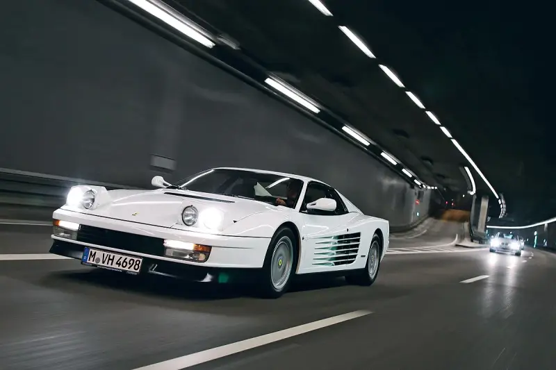 Weißer Ferrari Testarossa fährt durch einen beleuchteten Tunnel.